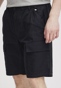 Zwarte cargoshorts van duurzame stof, met een elastische tailleband, zijzakken en een patchzak op het been.