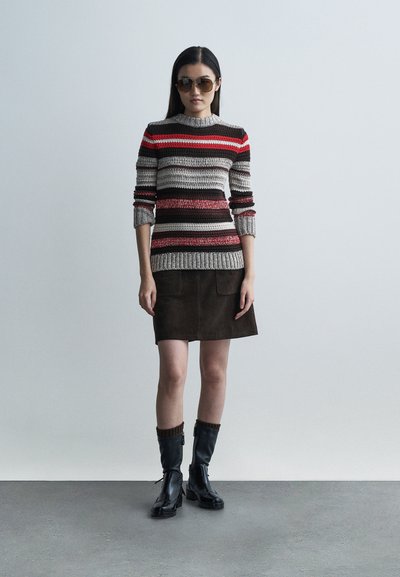 Sweter dziany z poziomymi czerwonymi, czarnymi i beżowymi paskami. Brązowa zamszowa spódnica z dwoma kieszeniami. Czarne skórzane botki z dzianymi mankietami.