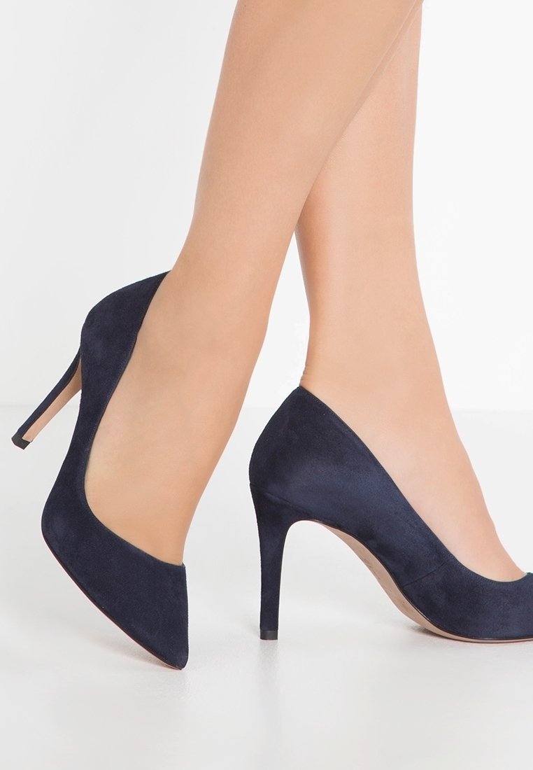 Mörkblå mocka högklackade skor med spetsig tå och en 10 cm hög stilettklack. Slät textur och minimalistisk design utan dekorationer.