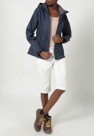 Chaqueta impermeable azul marino con capucha, camiseta beige, pantalones cortos cargo blancos y botas de senderismo marrones. Diseño texturizado con costuras y cremalleras visibles.