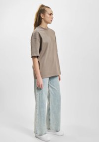Oversized light brown t-shirt with short sleeves, paired with wide-leg light blue jeans and white sneakers. Plain design with no patterns.