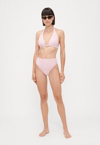 Bikini a righe rosa e bianche con scollo a halter, caratterizzato da un accento metallico circolare nella parte superiore e pantaloni a vita alta. Texture liscia.