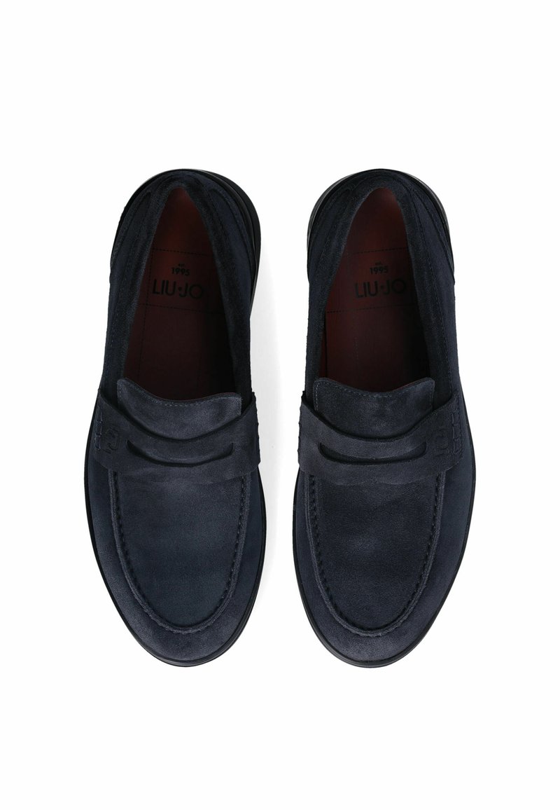 Mocasines de ante en color azul marino con un acabado suave, que presentan una tira decorativa en la parte frontal y una suela de goma. El forro interior es de color rojo oscuro.