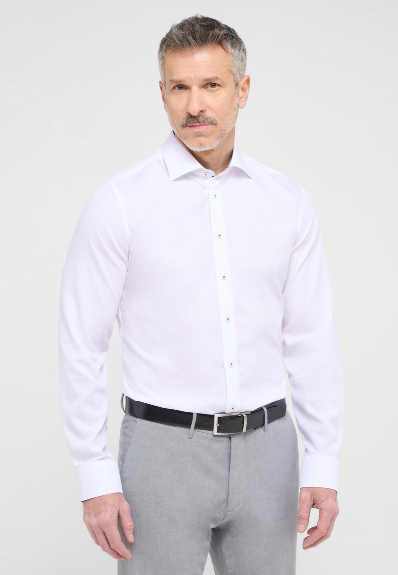Witte overhemd met lange mouwen, knoopsluiting en voorplacket, gecombineerd met grijze broek en een zwarte leren riem. Gladde stoftextuur.