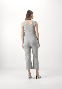 Grå bomulls jumpsuit med en tettsittende topp og vide avkappede ben, med belte i livet. Modellen har på seg sandaler med åpen tå og hæler.