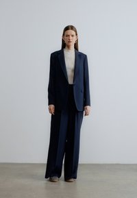 Navy tailored suit with a blazer and wide-legged trousers. The fabric appears smooth with structured shoulders and minimalistic design details.
