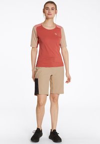 Kortärmad röd och beige skjorta med rund halsringning, kombinerad med beiga shorts som har en svart nätficka, lämplig för utomhusaktiviteter.