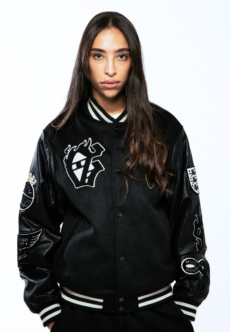 Chaqueta varsity negra con mangas de satén, cuello con rayas blancas y varios logotipos bordados en el pecho y las mangas.