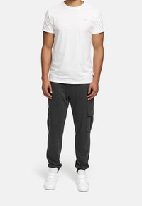 T-shirt blanc à col rond associé à un pantalon cargo sweatpants gris foncé avec poches latérales, porté avec des chaussures de sport blanches. Design simple et fonctionnel.