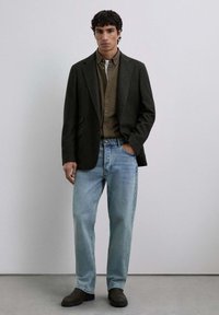 Conjunto informal que incluye un blazer oscuro, una camisa de cuadros verdes, jeans de color azul claro y zapatos negros sin cordones. Diseño simple y colores neutros.