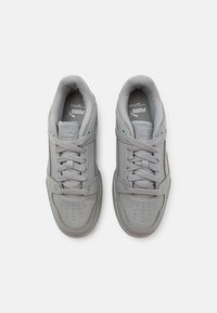 Un par de zapatillas Puma de color gris claro con cordones, área de puntera perforada y cuellos acolchados, vistas desde arriba sobre un fondo blanco.
