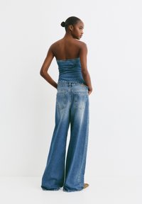 Denim top bez ramienok s priliehavým strihom, v kombinácii s vysokými, širokými džínami. Svetlomodrá farba s jemným opotrebovaním a detailmi z nitov.