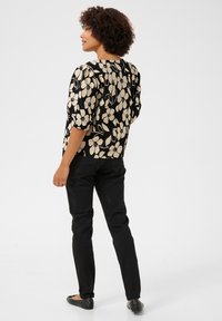 Blouse florale noire et dorée, col rond, manches bouffantes trois-quarts ; associée à un pantalon slim noir et des ballerines noires.