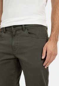 Dunkelgrüne Baumwollchinos mit geradem Schnitt, ausgestattet mit Eingrifftaschen, subtiler Textur und einem einzelnen Knopfverschluss an der Taille.