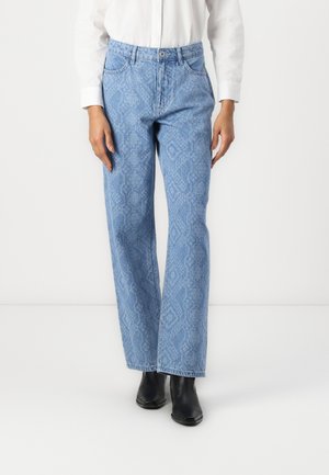 Jean en denim bleu clair avec un motif de peau de serpent, coupe droite, cinq poches et une fermeture à bouton, associés à des bottines noires.