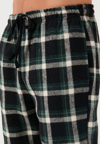 Geruite flanellen broek met een zwart, wit en groen kleurenschema, voorzien van een elastische tailleband en een verstelbaar trekkoord voor een goede pasvorm.