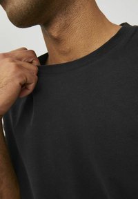 T-shirt nera a girocollo realizzata in cotone. Ingrandimento che mostra la morbida consistenza, la finitura liscia e una leggera elasticità nel colletto.
