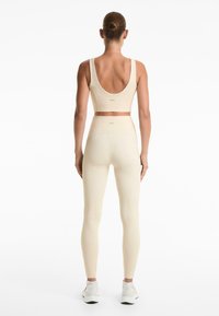Bežna atletska kombinacija koja uključuje uski crop top sa širokim trakama i tajice visokog struka, oboje u rebrastoj teksturi.