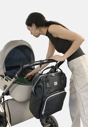 Cochecito de color gris claro con un interior azul oscuro. Bolso de pañales negro acolchado adjunto, con cremalleras y acentos plateados. Persona alcanzando dentro del cochecito.