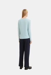 Light blue ribbed knit sweater with long sleeves, a scoop neckline, paired with dark navy wide-leg trousers and black shoes.