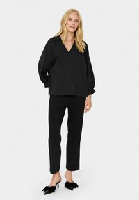 Black oversized blouse with a V-neck and long, voluminous sleeves, paired with tailored black trousers and black mules with bow accents.