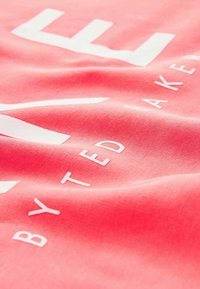 Tessuto corallo con una superficie liscia e la scritta bianca "TED BAKER" e la parola "LIFE" in evidenza, presentata in un carattere audace e moderno.