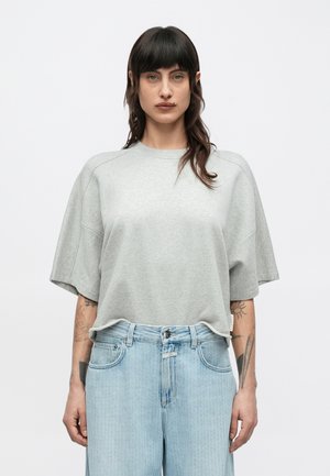 Ανοιχτό γκρι υπερμεγέθη μπλούζα από μαλακό ύφασμα, με στρογγυλή λαιμόκοψη και κοντά, φαρδιά μανίκια, συνδυασμένη με ανοιχτό μπλε τζιν παντελόνι.