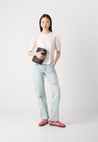 Tricou alb cu mâneci bufante din dantelă, blugi deschiși la culoare, rupți, adidași roz cu accente albe și o poșetă neagră.