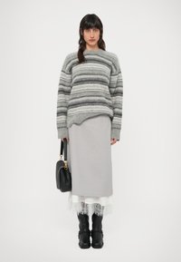 Sivi prugasti vuneni džemper opuštenog kroja, uparen sa svijetlosivom midi suknjom i crnim čizmama koje sežu do koljena. U ruci se drži crna torba.