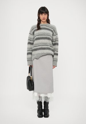 Sivý pruhovaný vlnený sveter s voľným strihom, skombinovaný so svetlosivou midi sukňou a čiernymi čižmami nad kolená. V ruke sa drží čierna kabelka.