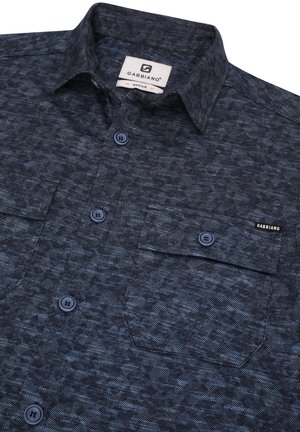 Camisa de botones azul oscuro con un patrón texturizado, que cuenta con dos bolsillos en el pecho, botones en contraste y una etiqueta con el nombre de la marca.