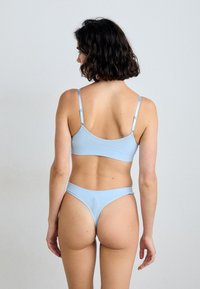 Ljusblå rippad bikini-set med en cropped topp med tunna justerbara axelband och låg midja thong-bakdelar, som visar en slät textur.