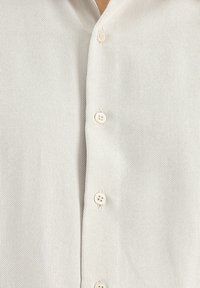 Camicia button-up beige chiaro realizzata in un tessuto testurizzato, con cinque bottoni sulla parte frontale e un design con colletto classico.