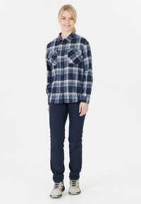 Navy und hellblauschottierte Flanellhemd mit zwei Brusttaschen, kombiniert mit dunkelblauen Hosen und beigen Wanderschuhen. Weiche Stofftextur.