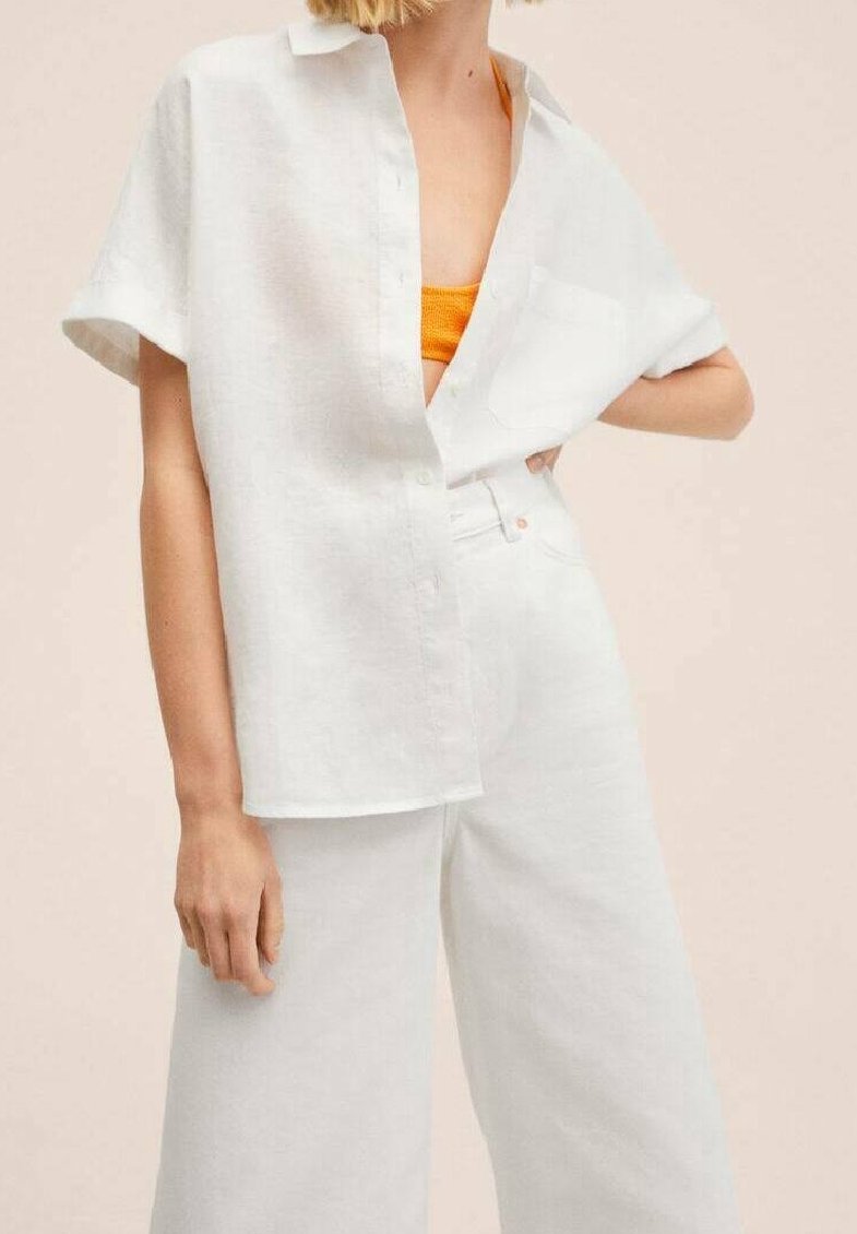 Chemise blanche en lin à manches courtes, boutonnée à l'avant, avec une poche sur la poitrine, associée à un pantalon blanc à jambes larges et un débardeur orange en dessous.