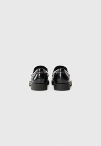 Black leather shoes with a smooth finish, rounded toe, and thick sole. Features a silver buckle detail on a strap across the instep.