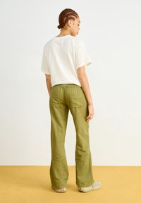 Lightweight, green linen pants with a relaxed fit, elastic waistband, and two back pockets, paired with a loose-fitting, white cotton T-shirt.