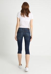 Jeans i denim capri-stil i mörkblått, med en åtsittande design, midjehöjd och avskuren längd, samt bakfickor med en läderetikett som accent.