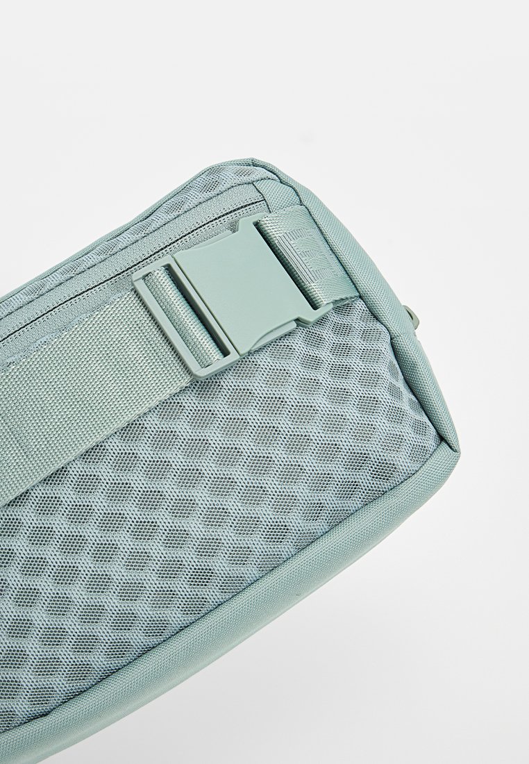 Esquina de bolsa de tela verde claro con patrón de malla hexagonal, hebilla lateral de plástico a juego y una correa ajustable.