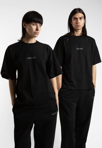 Black oversized t-shirts with a round neckline, featuring reflective "wasted" logo centered on the chest. Worn with matching black pants.