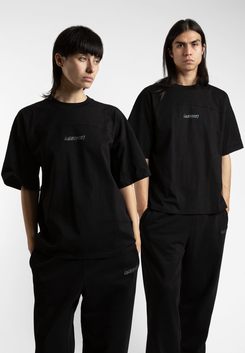 Black oversized t-shirts with a round neckline, featuring reflective "wasted" logo centered on the chest. Worn with matching black pants.