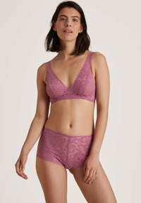 Set di bralette e shorts in pizzo di un vivace rosa, con un design scallop e un motivo floreale. Texture morbida e dettagli in tessuto delicato.
