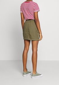 Röd- och vitrandig kortärmad topp parat med en khakigrön minikjol med elastisk midja och sidofickor. Grå sneakers.