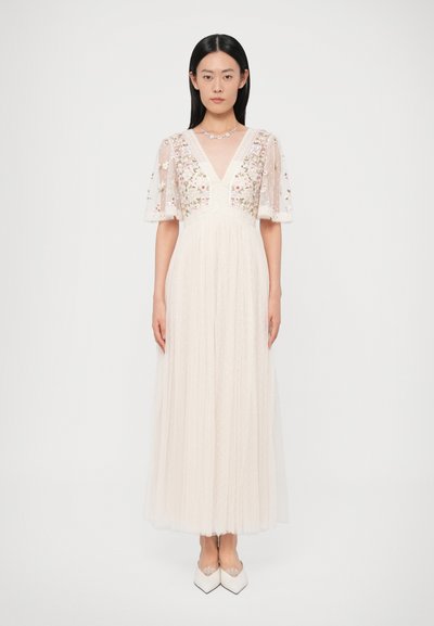 Longue robe ivoire avec manches transparentes brodées, décolleté en V et corsage texturé. Une jupe fluide en tulle présente un motif à pois.