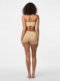 Beige saumatön bikini ja poissümont, õhukeste rihmadega ja sileda tekstuuriga, disainitud tihedalt kehale sobima.