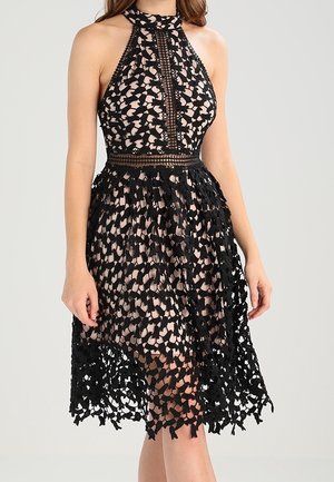 Sleeveless halter neck midi dress with black floral lace overlay and nude underlayer, fitted waist, and scalloped hem.