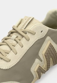 Μπεζ αθλητικό παπούτσι με υφασμάτινο γκρι πάνελ, ενισχυμένη μύτη και μαλακά κορδόνια. Διαθέτει λαστιχένια σόλα με σχέδια πρόσφυσης και την επωνυμία "Merrell".