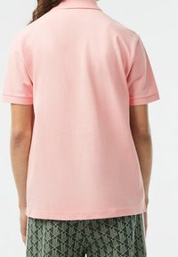Polo rose avec un tissu texturé, manches courtes et col classique. Porté avec un pantalon vert à motifs.