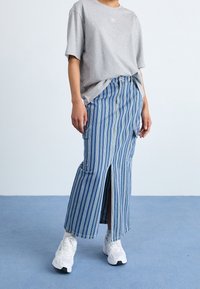Gonna di jeans a righe con spacco frontale, caratterizzata da righe verticali blu e bianche, abbinata a una t-shirt oversize grigia e sneakers bianche.