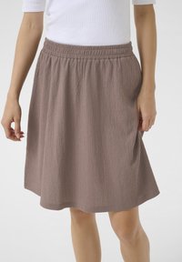 Une jupe légère, jusqu'aux genoux, dans une teinte mauve atténuée. Dotée d'une taille élastique et d'un tissu texturé avec des ondulations subtiles.